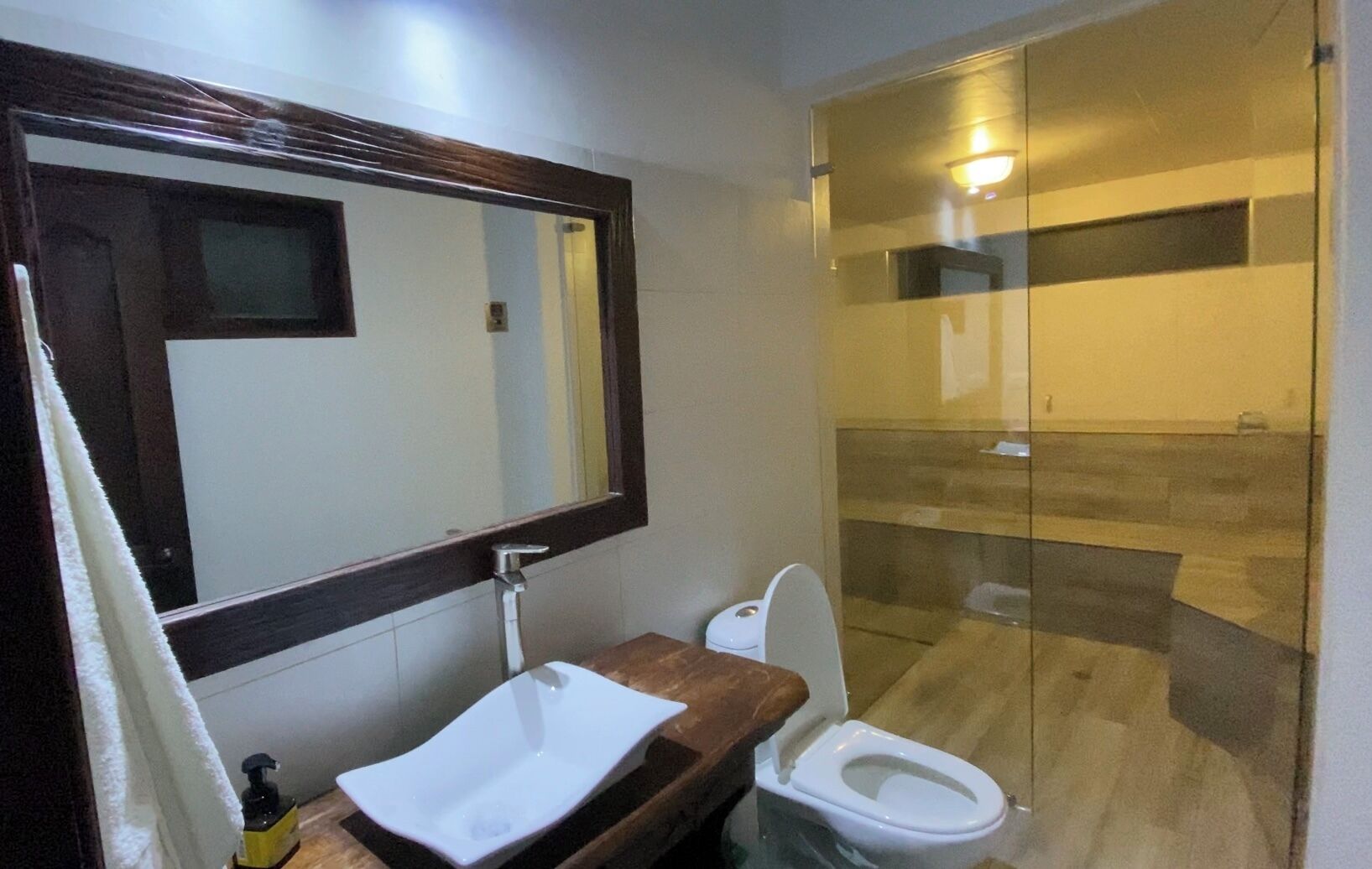 Een badkamer met een houten wastafelmeubel, een witte wastafel, een toilet en een douchecabine met glazen wanden.