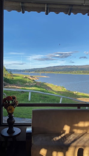 Une pièce avec vue sur un lac et des collines, une chaise et un vase de fleurs posé sur une table.