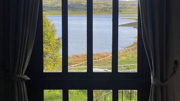 Una ventana con cortinas, vista a un lago y una zona ajardinada con valla.