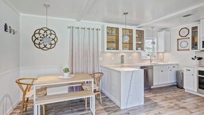 Una cucina moderna con mobili bianchi, un'isola in marmo e un'area pranzo con tavolo e sedie in legno.