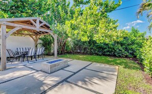 Eine Terrasse im Freien mit einer Holz-Pergola, einem Tisch mit Stühlen und einem Beton-Pflanzgefäß.