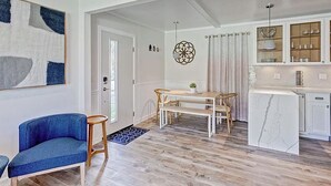 Un'ampia zona giorno con tavolo da pranzo, un divano blu e una cucina con pensili e zoccolo in marmo.