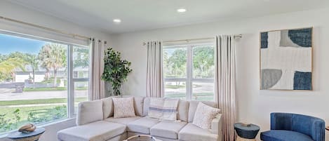 A spacious living room with a large sectional sofa, a blue armchair, and a woven coffee table.