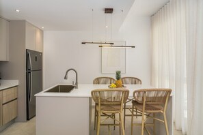 A modern kitchen with a built-in island, stainless steel appliances, and a dining area with wicker chairs. - Ground-floor 1BR at Mareal • Walk to the Beach (Cabarete)