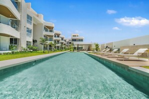 A modern hotel with a swimming pool, outdoor seating, and a clear blue sky. - Ground-floor 1BR at Mareal • Walk to the Beach (Cabarete)