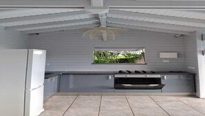 Uma cozinha com geladeira branca, janela com vista para vegetação e teto com vigas aparentes.