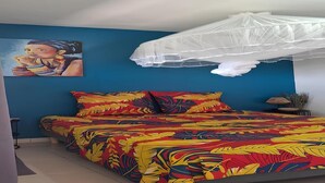 Quarto com uma cama, mosquiteiro, pintura na parede e planta na mesinha de cabeceira.