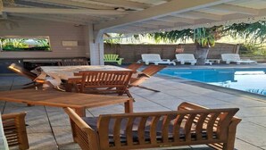 Um pátio ao ar livre com piscina, móveis de madeira e uma tela de televisão.