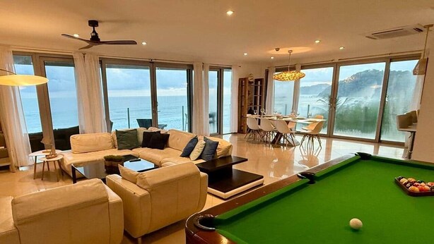 Ein modernes Wohnzimmer mit Billardtisch, Sitzecke und großen Fenstern mit Meerblick.