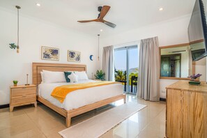 A modern bedroom with a wooden bed, a ceiling fan, and a view of the outdoors through a sliding glass door. - Diamante 701n - Downtown Jaco Deluxe Penthouse (Jaco)