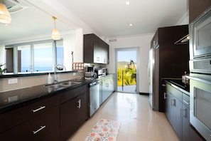 A modern kitchen with a large window, stainless steel appliances, and a view of the ocean. - Diamante 701n - Downtown Jaco Deluxe Penthouse (Jaco)