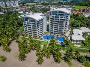 Ein Hochhaus-Hotel mit mehreren Balkonen, einem Swimmingpool und einer Strandanlage mit Palmen.