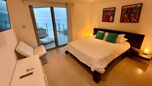 Ein Hotelzimmer mit Bett, Schreibtisch, Stuhl und einem Balkon mit Blick aufs Meer, sowie Kunstwerken an der Wand.