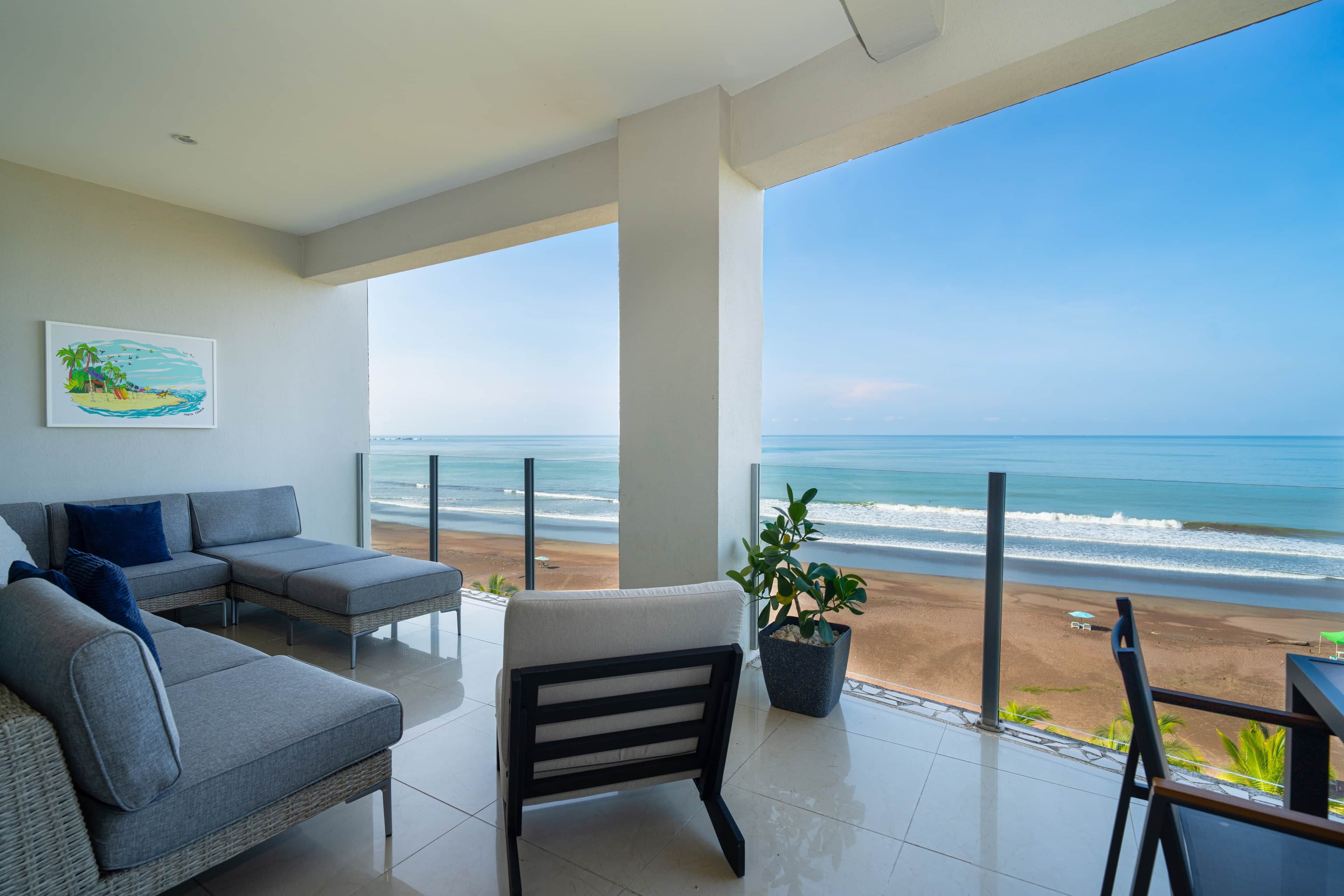 Ein Balkon mit Blick auf den Strand, eine Couch, ein Sessel und ein Blumentopf.