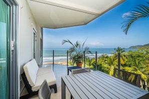 A balcony with a view of the ocean, a table, chairs, and a potted plant. - Diamante 701n - Downtown Jaco Deluxe Penthouse (Jaco)