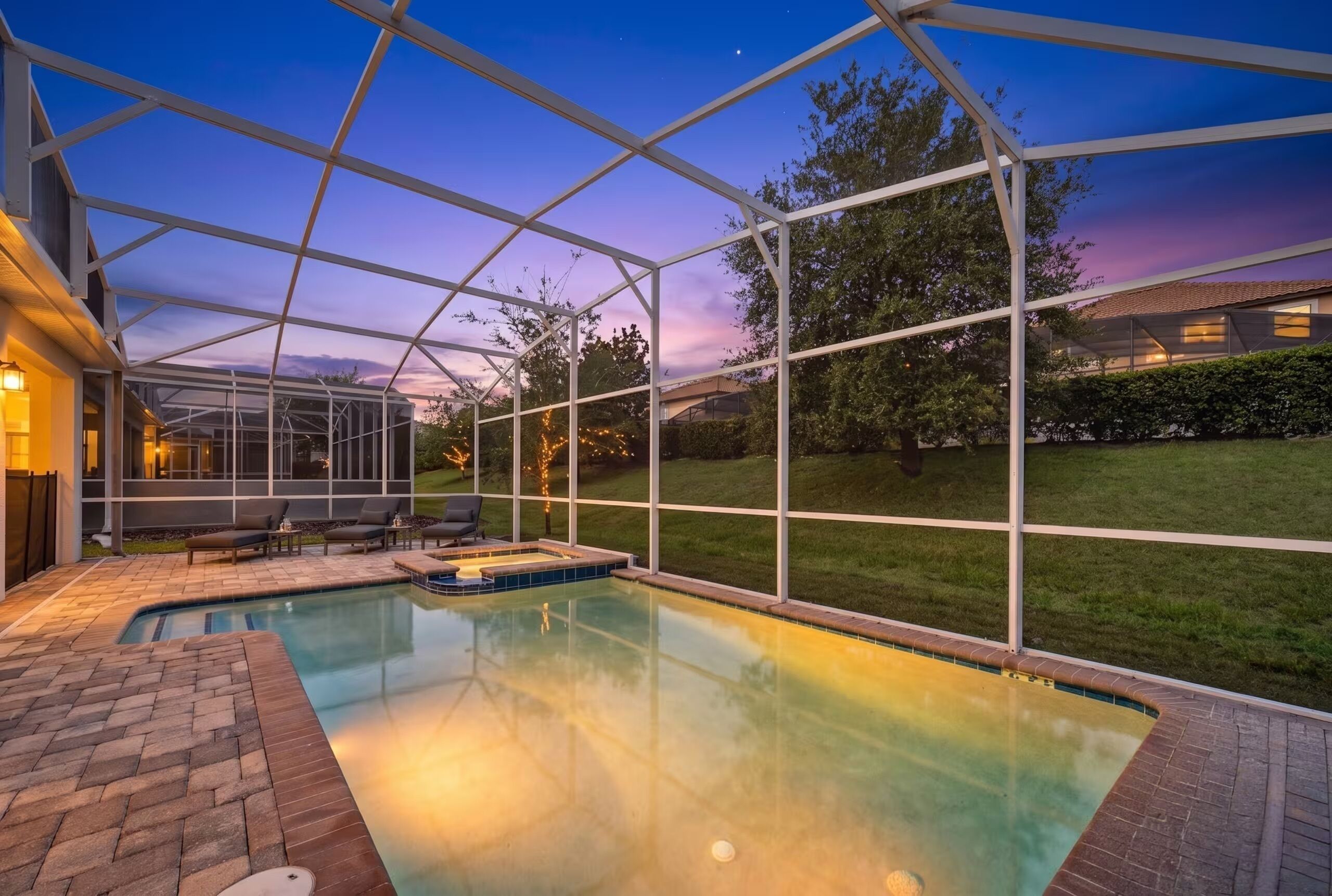 A swimming pool with a glass enclosure, a brick patio, and a view of the surrounding landscape.