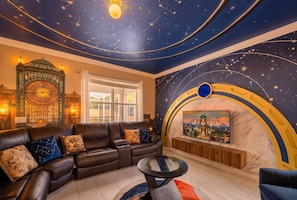 A room with a starry ceiling, a sofa with cushions, a round table, and a TV mounted on a wall with a circular design. - The Epic Escape Mansion near Disney/Universal •Free Parking •5-Baths •25 Guests (Four Corners)