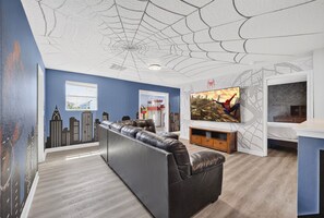 A modern living room with a sofa, a TV, and a cityscape mural on the wall. - The Epic Escape Mansion near Disney/Universal •Free Parking •5-Baths •25 Guests (Four Corners)