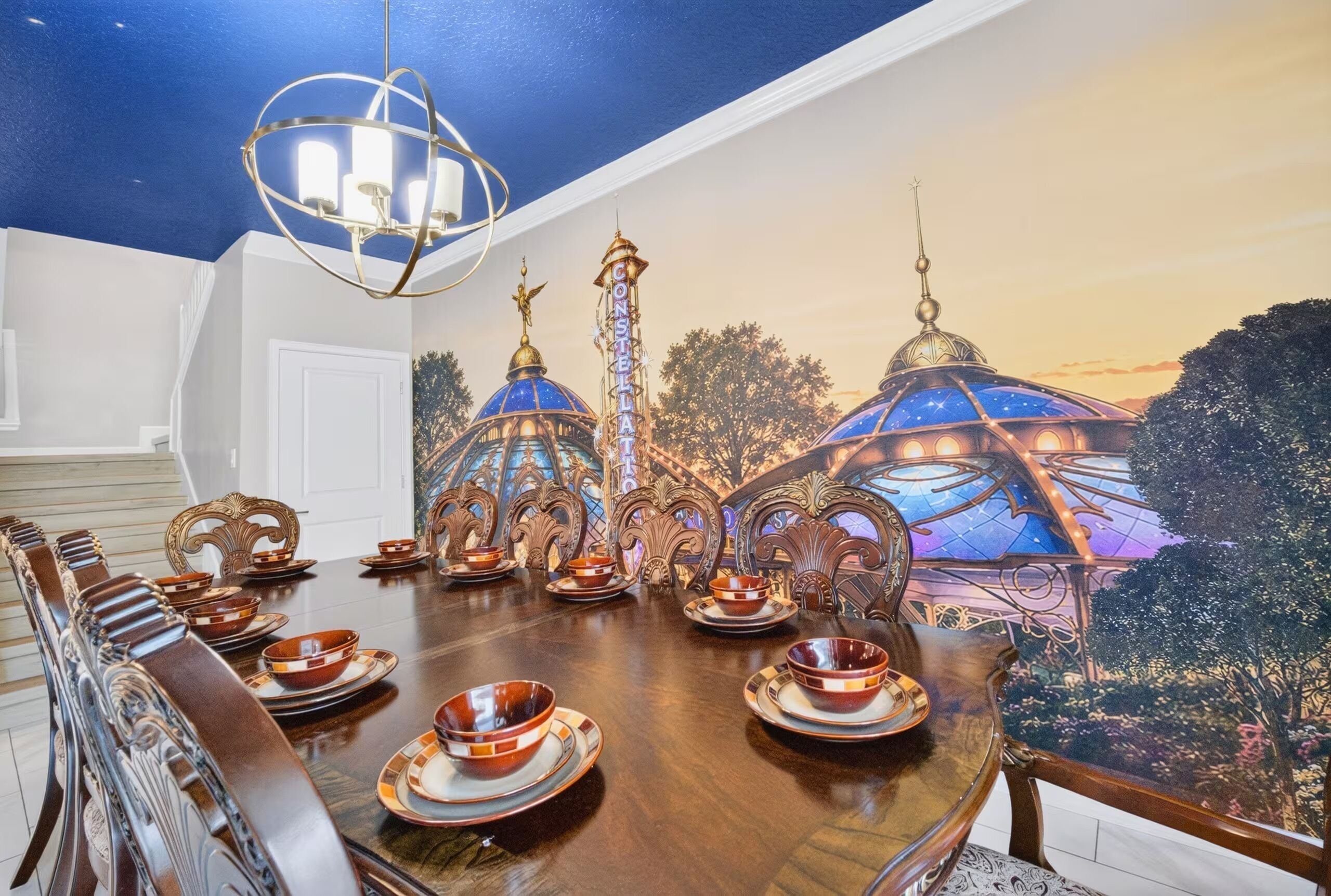 A dining area with a large table set for a meal, ornate chairs, and a ceiling mural depicting a celestial scene.