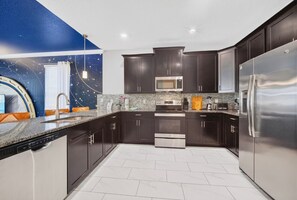 Une cuisine moderne avec des meubles de couleur sombre, des appareils en acier inoxydable et un revêtement mural décoré de motifs étoilés.
