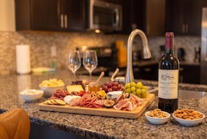 A charcuterie board with various meats, cheeses, fruits, and nuts on a kitchen counter, accompanied by a bottle of wine and glasses. - The Epic Escape Mansion near Disney/Universal •Free Parking •5-Baths •25 Guests (Four Corners)