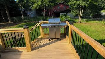 A wooden deck with a barbecue grill, surrounded by a metal fence and trees.