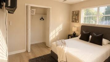A bedroom with a bed, a ceiling fan, a nightstand, a lamp, a closet, and a window with blinds.