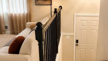 A bedroom with a bed, a nightstand, a lamp, a painting, a door, and a staircase.