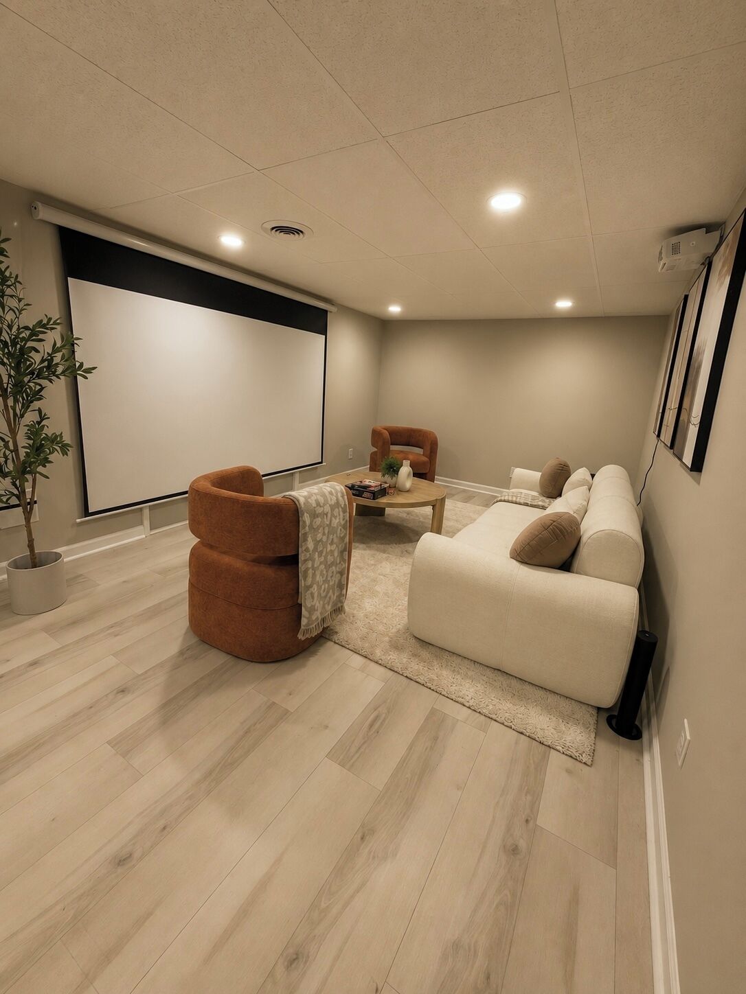 A home theater room with a large screen, comfortable seating, and a wooden floor.
