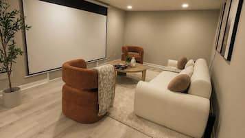 A home theater room with a large screen, comfortable seating, and a wooden floor.