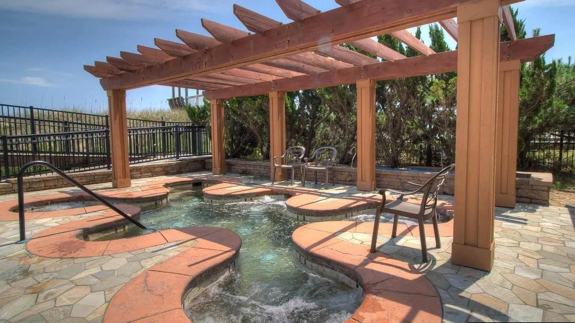 Een hottubgedeelte met een houten pergola, stenen trappen en buitenmeubilair.