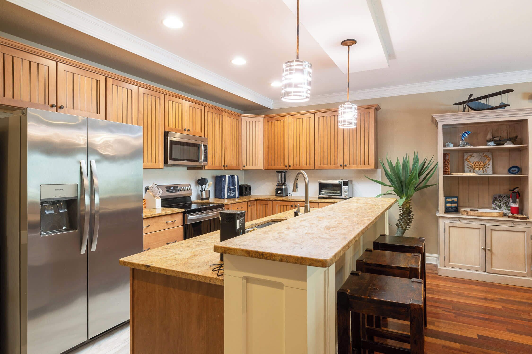 A modern kitchen with wooden cabinets, stainless steel appliances, a central island, and pendant lighting.