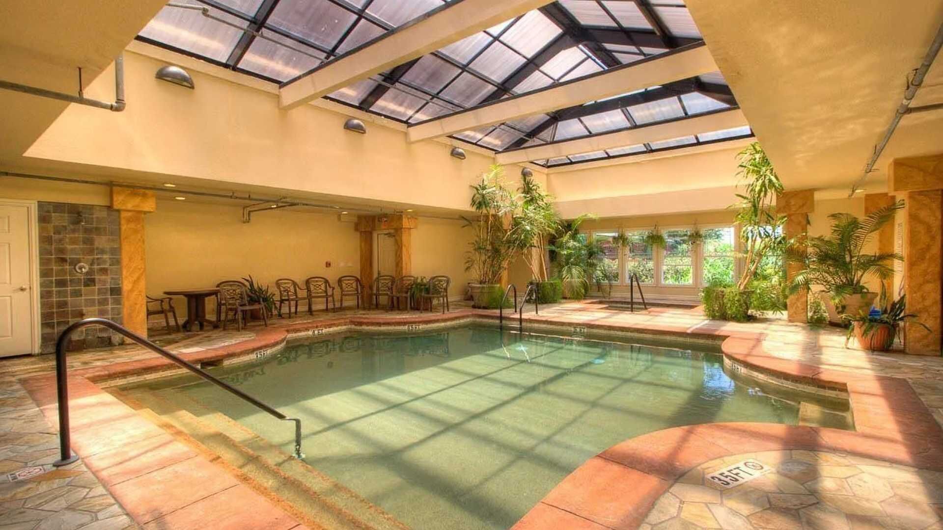 Una piscina interior con techo de cristal, rodeada de sillas y plantas en macetas.