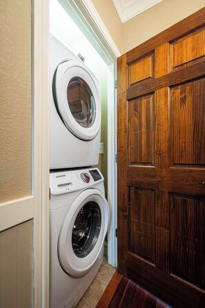 Une buanderie avec des machines à laver et des sèche-linge superposés, une porte en bois et un interrupteur sur le mur.