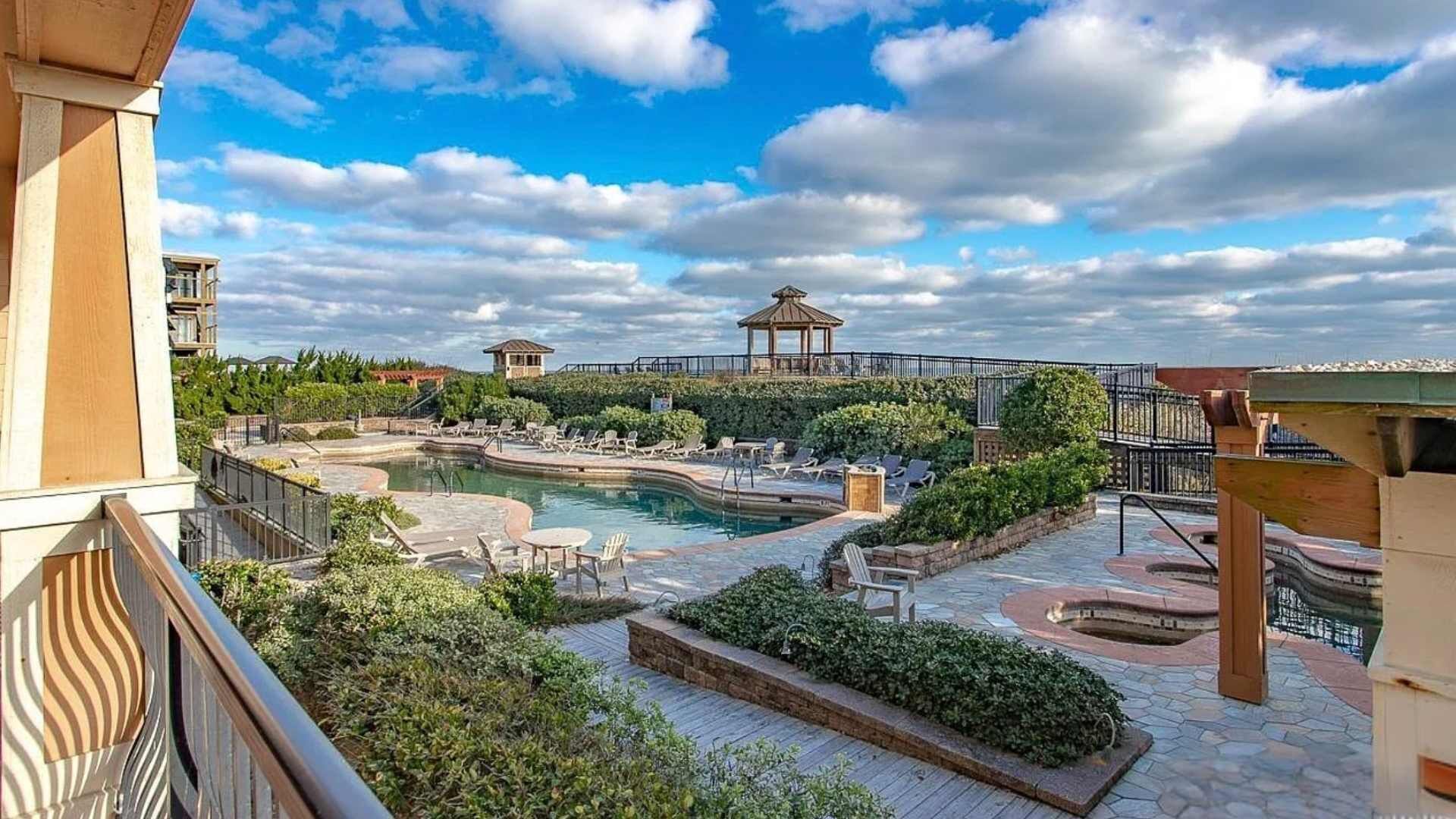 A rooftop pool area with lounge chairs, a gazebo, and a view of the sky.
