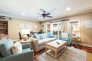 A living room with a sofa, armchairs, a coffee table, a ceiling fan, and a dining area with a table and chairs.