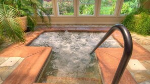A hot tub with a metal ladder, surrounded by stone tiles and potted plants.