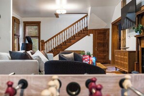 Un salón con escalera de madera, un sofá, una mesa de centro y una estantería.