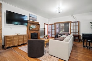 Una sala de estar con televisión, chimenea, sofá, reposapiés y piano.