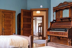 Una habitación con una cama, un piano de madera y una puerta que da a otra estancia.