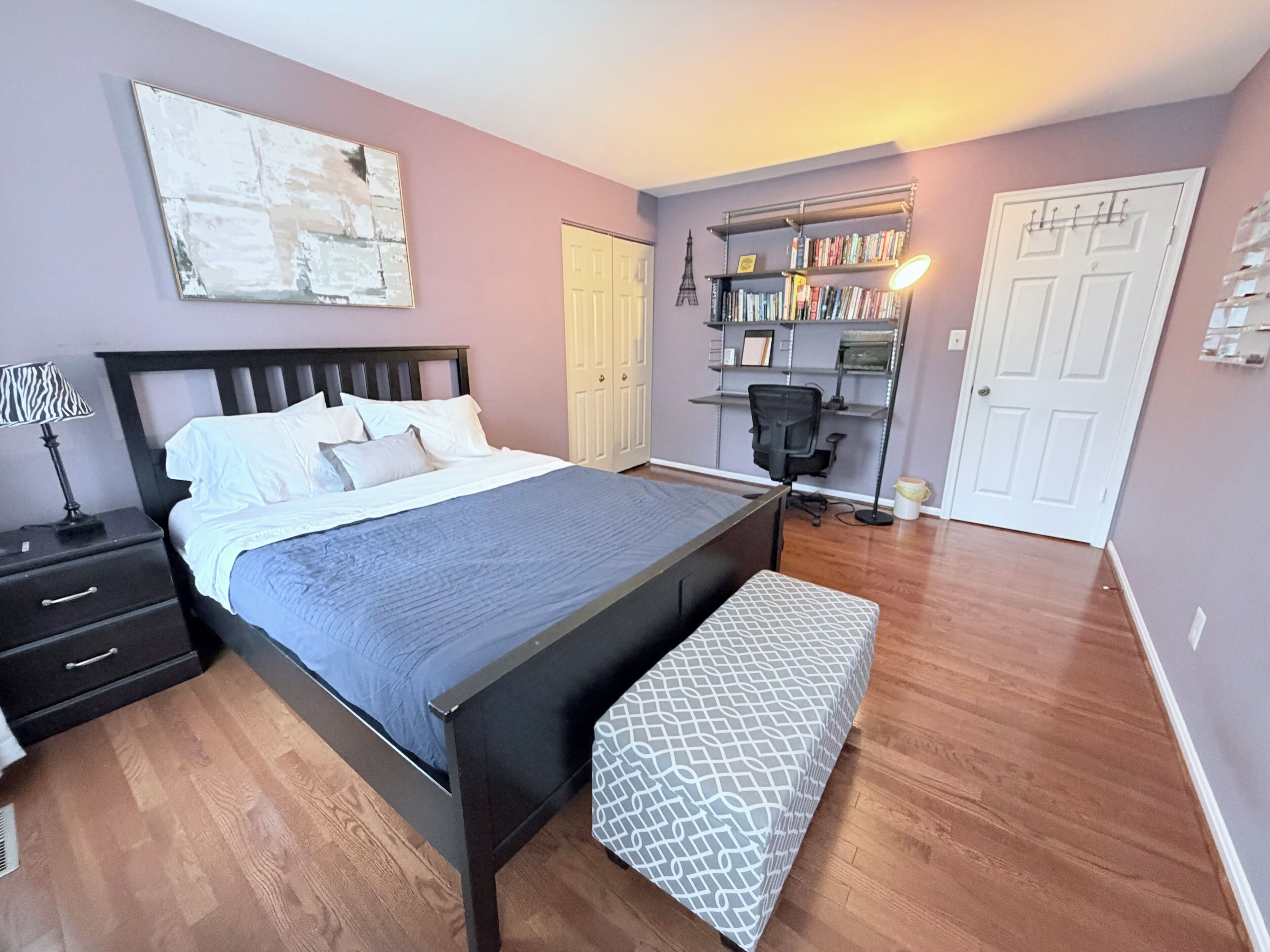 A bedroom with a bed, bedside table, lamp, bookshelf, and a desk with chair.