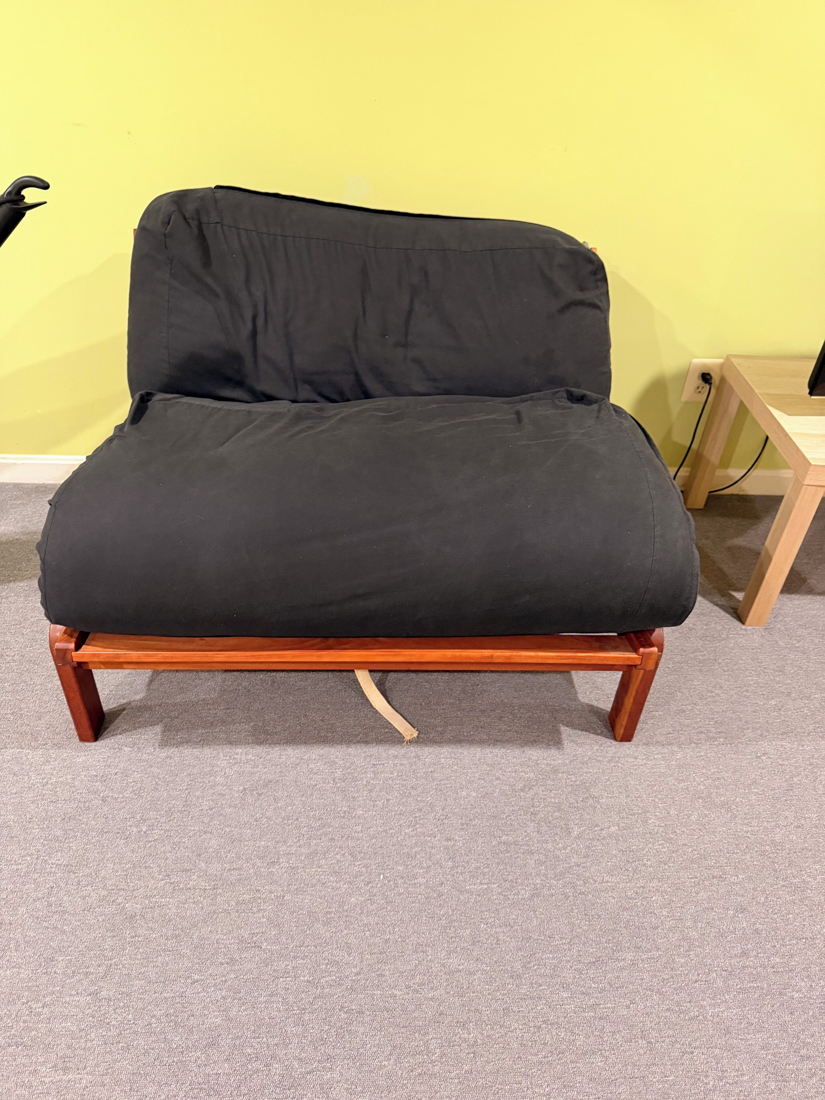 A black sofa with wooden legs against a yellow wall.