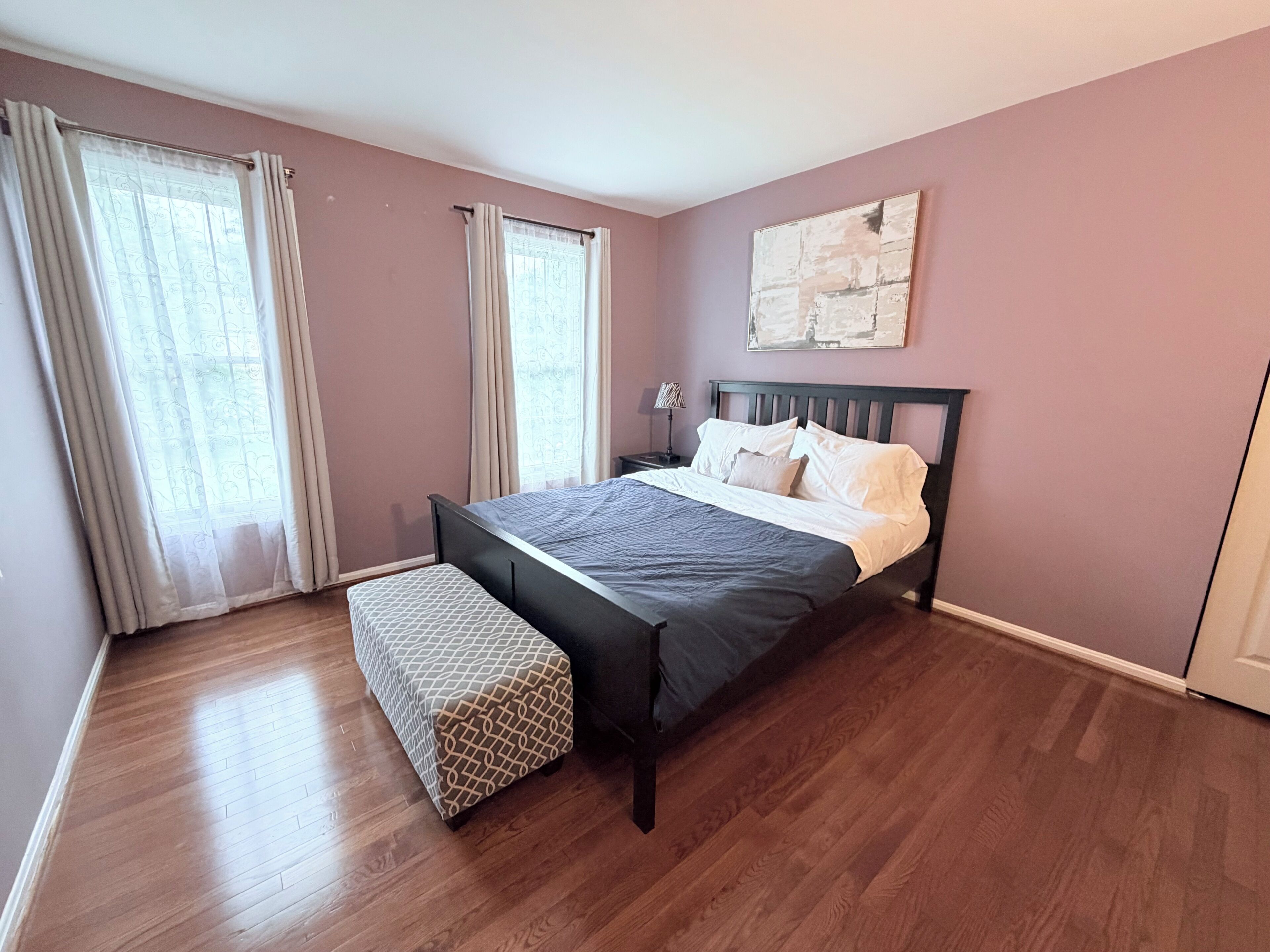 A bedroom with a bed, a nightstand, a lamp, and a bench.