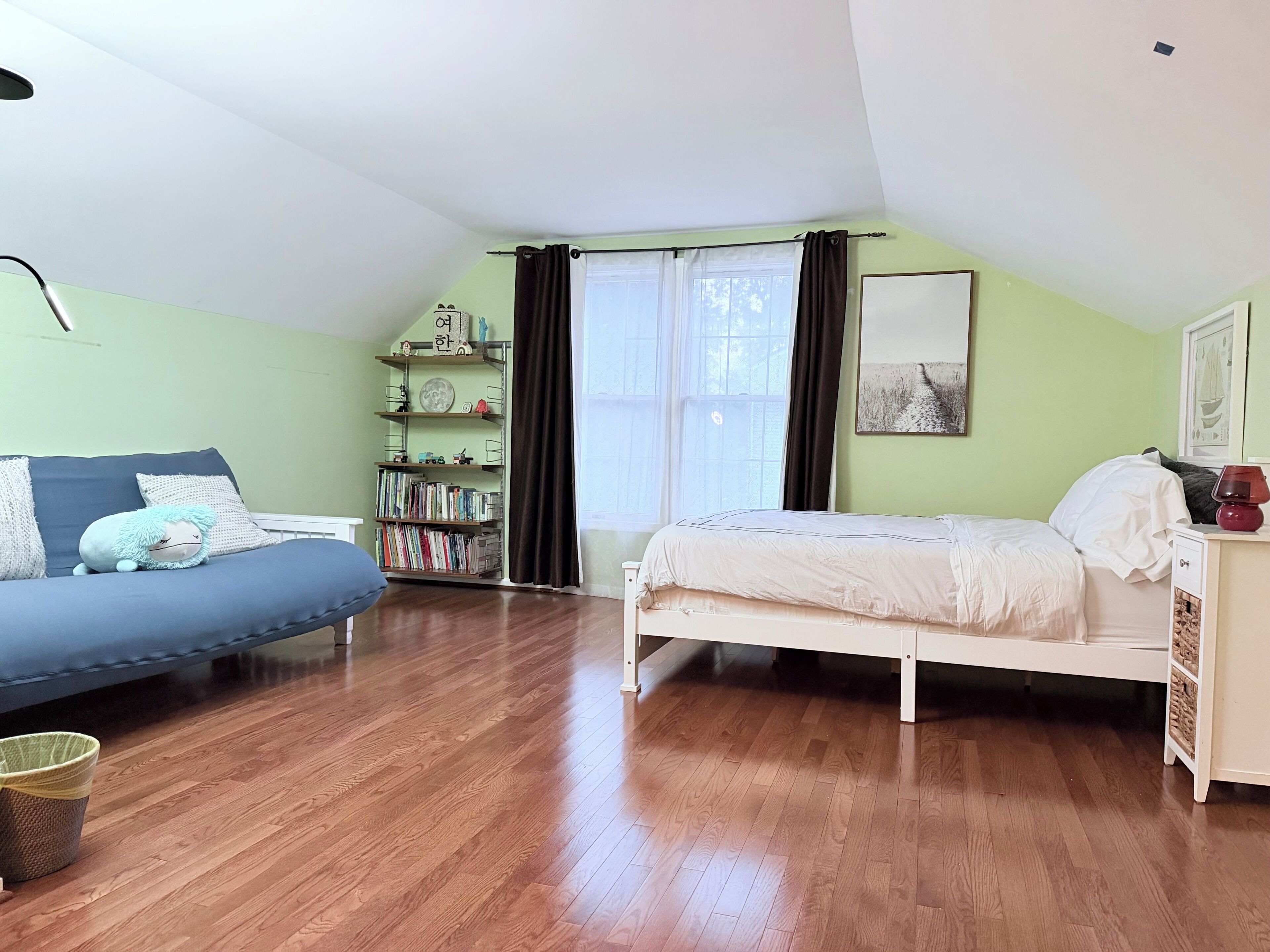 Una habitación con una cama, un sofá, una estantería y una ventana con cortinas.