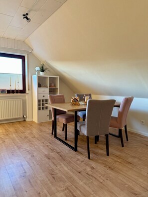 A dining area with a table and chairs, a radiator, a white cabinet with drawers, and a window with blinds. - Ferienwohnung Wildblume Meißner - Erholung im Meißnervorland (Meißner)