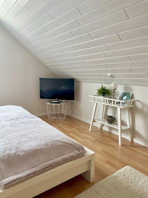 A bedroom with a bed, a desk with a plant, a TV, and a white ceiling. - Ferienwohnung Wildblume Meißner - Erholung im Meißnervorland (Meißner)