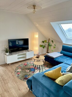 A modern living room with a flat-screen TV, a blue sofa, a round coffee table, and a skylight. - Ferienwohnung Wildblume Meißner - Erholung im Meißnervorland (Meißner)