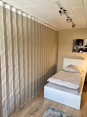Een slaapkamer met een bed, gordijnen, een plafondlamp en een aan de muur hangend schilderij.