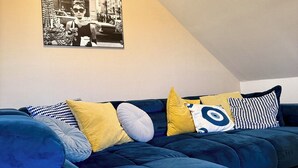 Ett modernt vardagsrum med en blå hörnsoffa, en gul kudde och ett svartvitt fotografi på väggen.