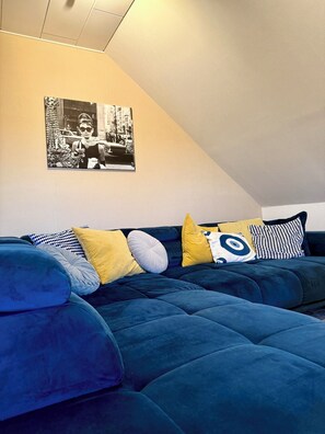 A modern living room with a blue sectional sofa, a yellow pillow, and a black-and-white photograph on the wall. - Ferienwohnung Wildblume Meißner - Erholung im Meißnervorland (Meißner)